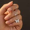Silver butterfly necklace held by a hand against a dark background