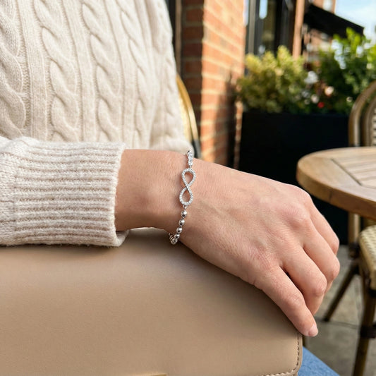 Person wearing a silver bracelet with an infinity symbol on a blurred outdoor background