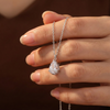 Hand holding a silver necklace with a teardrop-shaped diamond pendant against a dark background