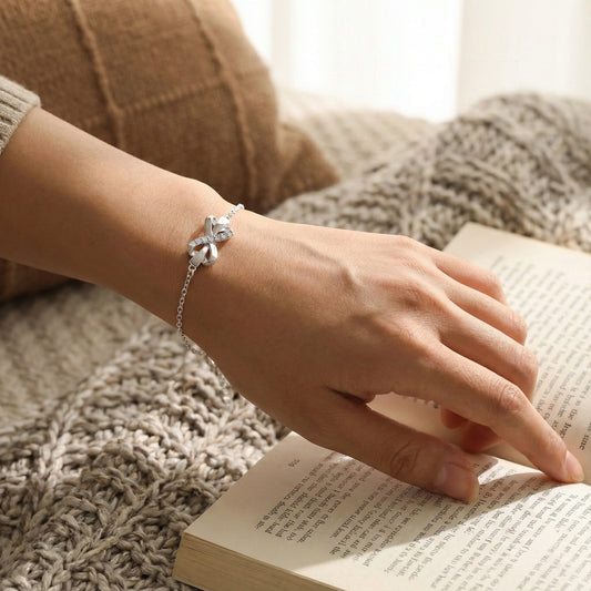 Person's hand wearing a silver bracelet on an open book, with a cozy background.