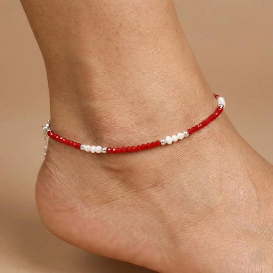 Red beaded anklet on a person's ankle against a beige background