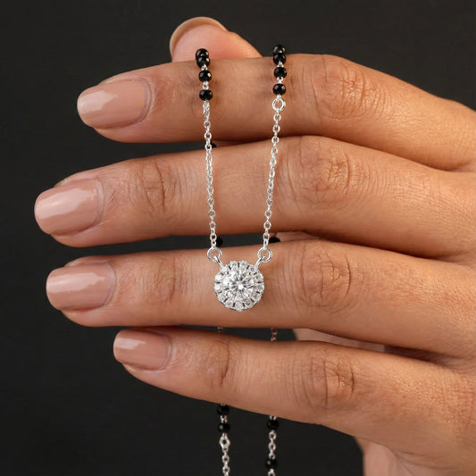 Hand holding a silver necklace with a round pendant against a dark background