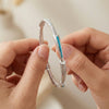 Close-up of hands holding a silver bracelet with a blue accent against a neutral background