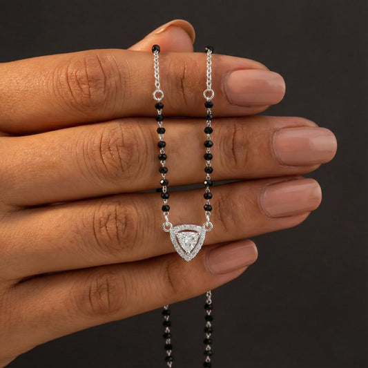 Hand holding a necklace with a black beaded chain and silver clasp against a dark background