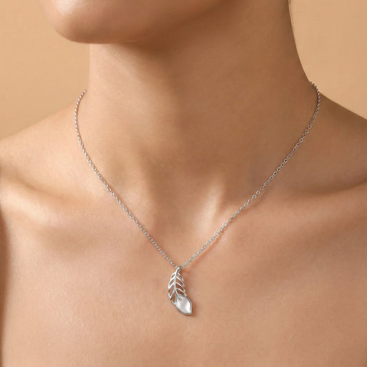 Silver necklace with a leaf pendant on a person's neck against a beige background