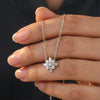 Silver necklace with a diamond pendant held between fingers against a dark background