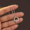 Silver necklace with a circular pendant held by a hand against a dark background