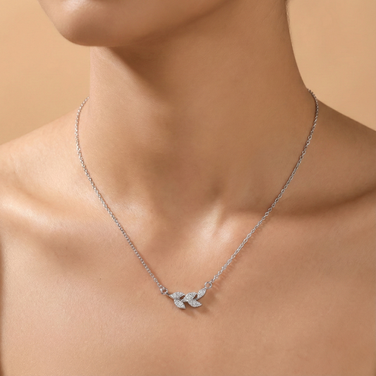 Silver necklace with a leaf pendant on a person against a beige background