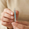 Close-up of hands holding a diamond ring with blue gemstones against a beige background