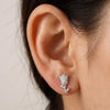 Silver rose-shaped earring worn on an ear with a neutral background