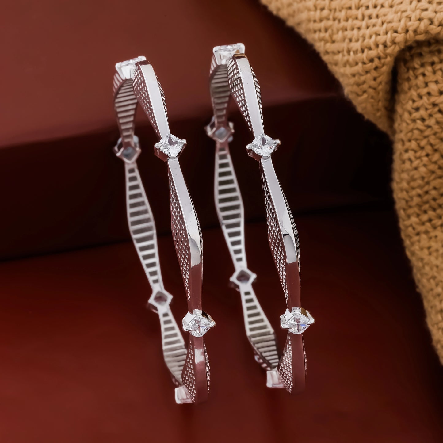 Pair of silver hoop earrings with diamond-like stones on a brown background