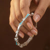 Silver bracelet with turquoise accents and diamond-like stones held by a hand against a dark background