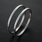Two silver bangles with gemstone accents on a dark textured background