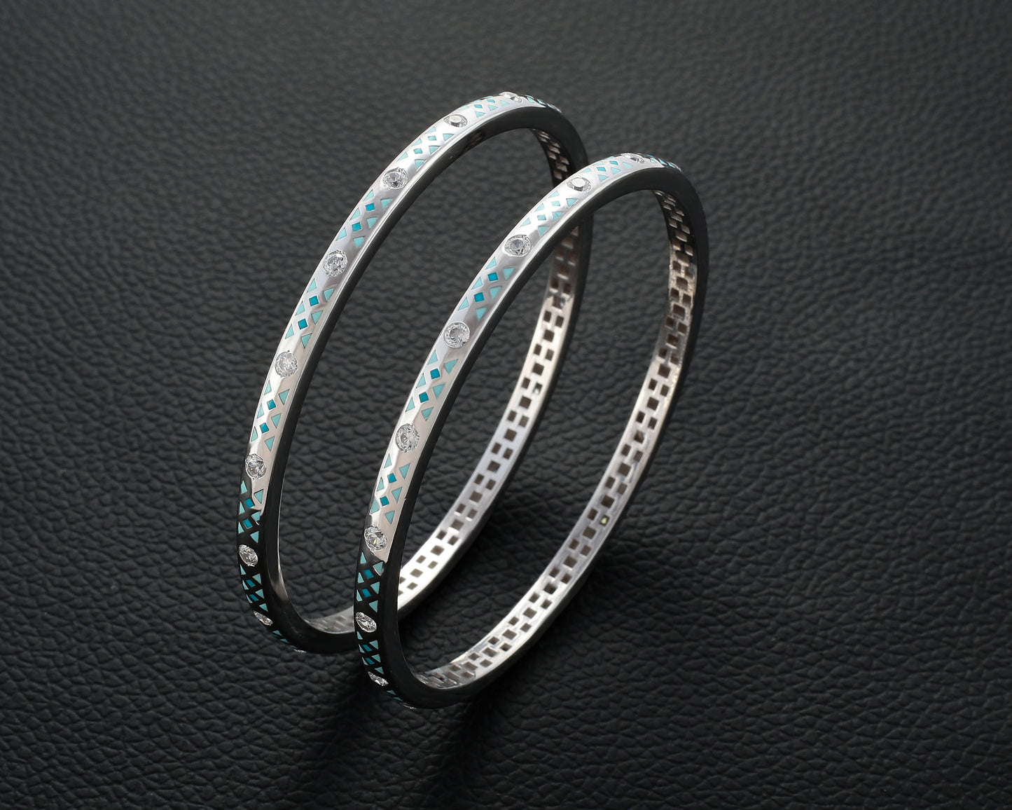 Two silver bangles with gemstone accents on a dark textured background