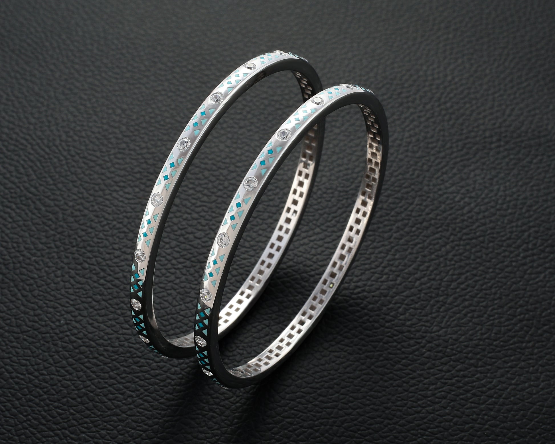 Two silver bangles with gemstone accents on a dark textured background