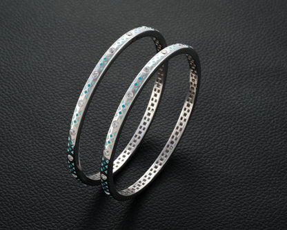 Two silver bangles with gemstone accents on a dark textured background