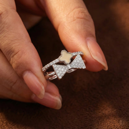 Silver ring with bow design held between fingers on a brown background