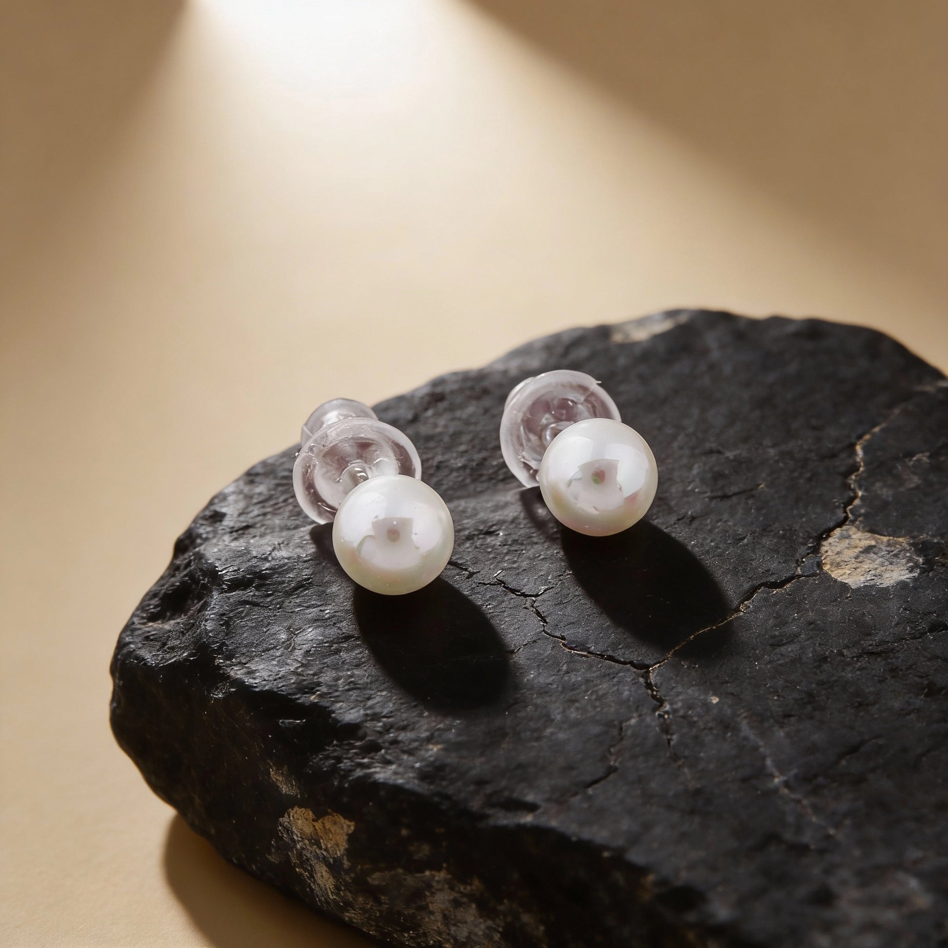 Pearl earrings on a dark stone surface with a warm light background