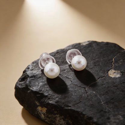 Pearl earrings on a dark stone surface with a warm light background