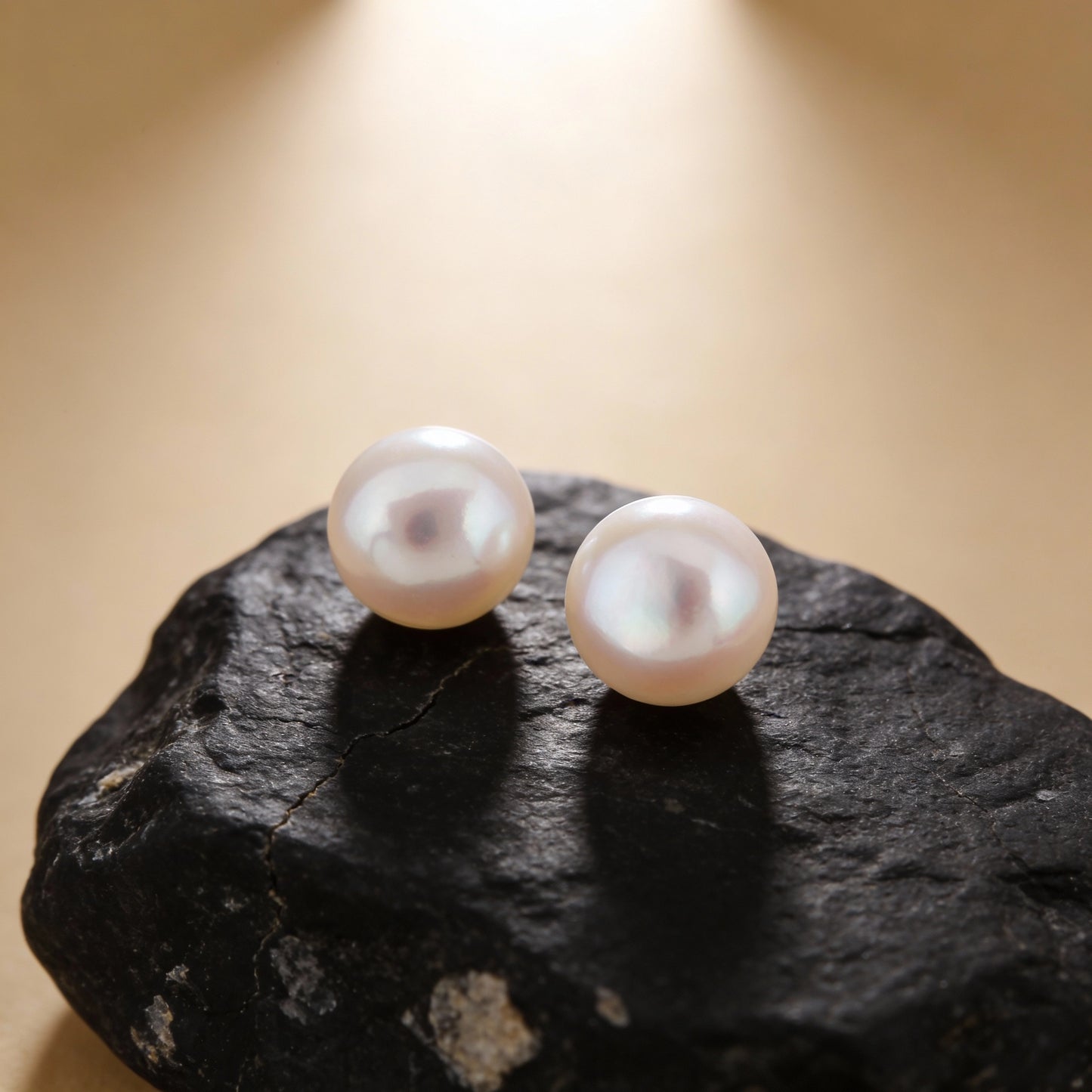 Pearl earrings on a dark stone surface with a beige background