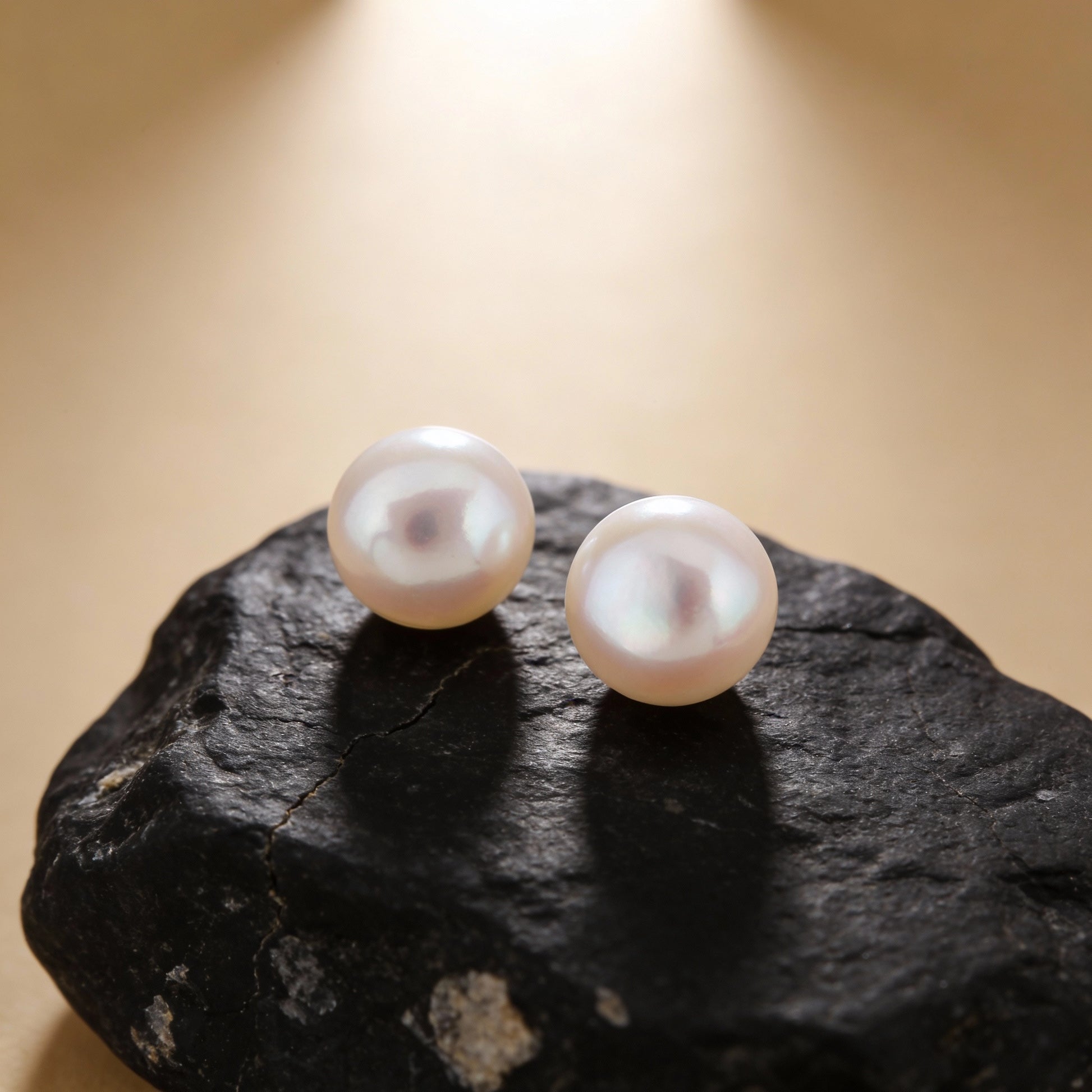 Pearl earrings on a dark stone surface with a beige background