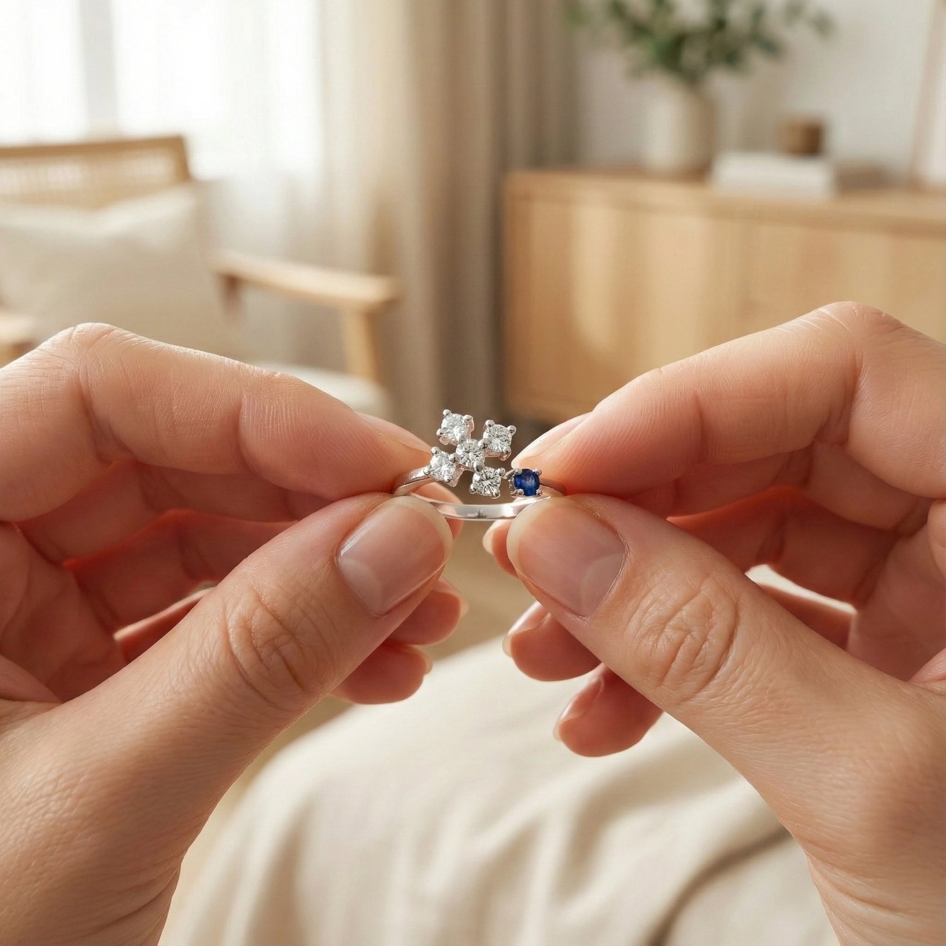 Close-up of hands holding a diamond ring with a blue gemstone in a softly lit room.