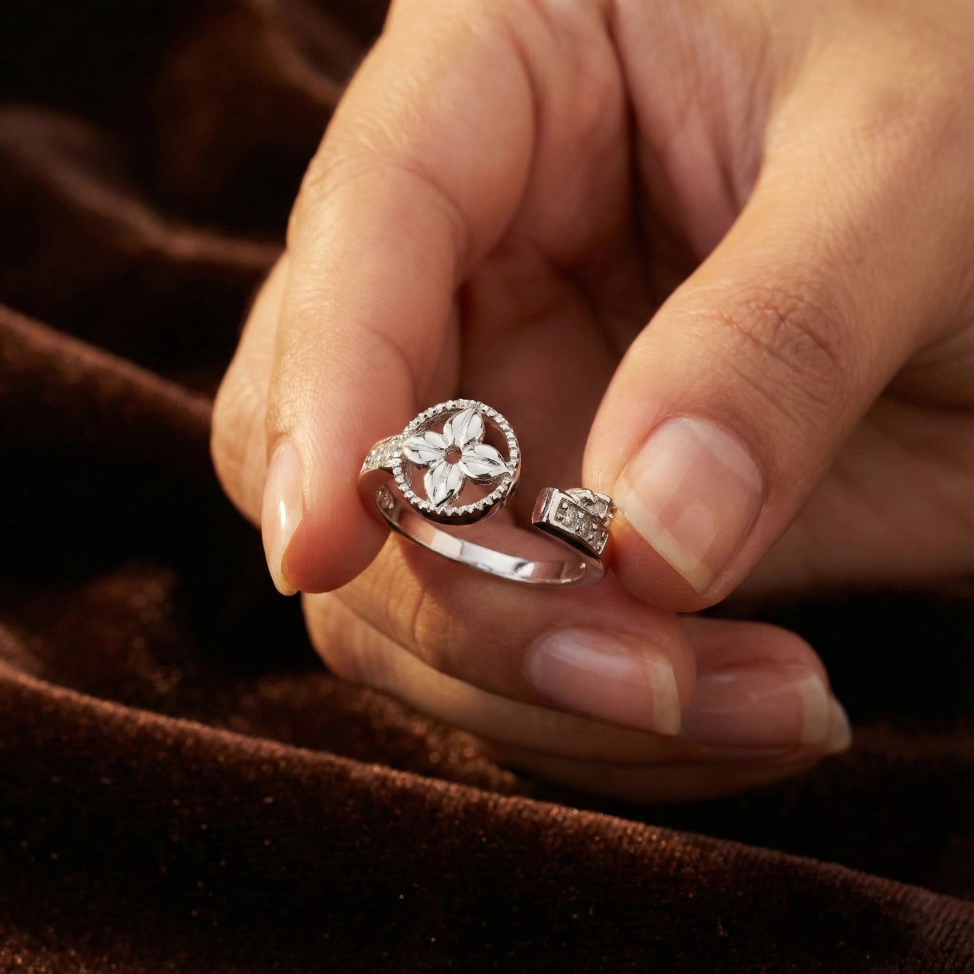 Close-up of a hand holding two silver rings with intricate designs against a brown fabric background.