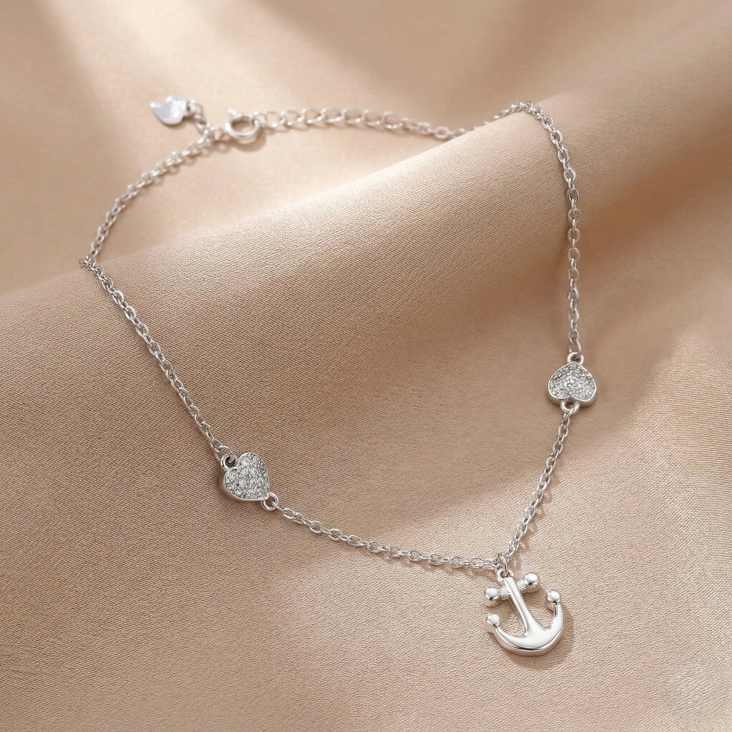 Silver anklet with anchor charm on a beige background