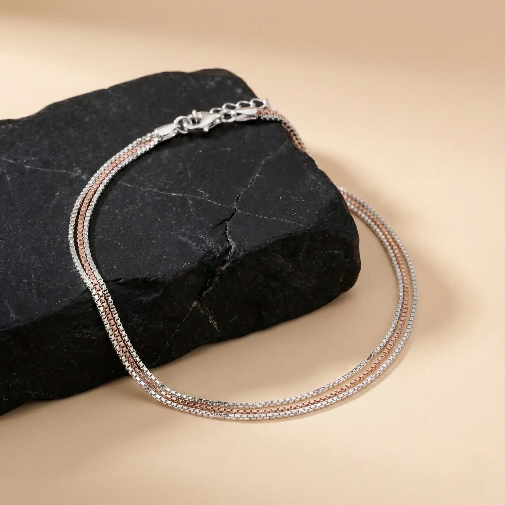 Silver and rose gold chain necklace on a black stone with a beige background