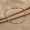 Beaded bracelet with red and white stones on a beige fabric background