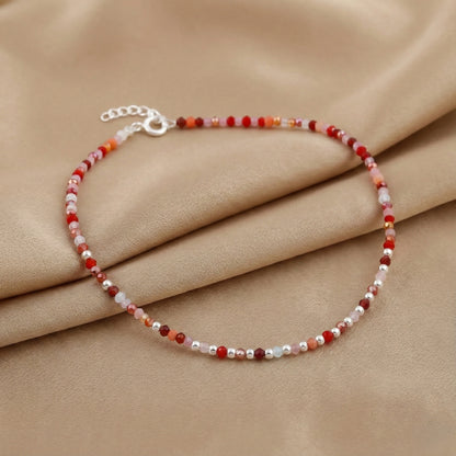 Beaded bracelet with red and white stones on a beige fabric background