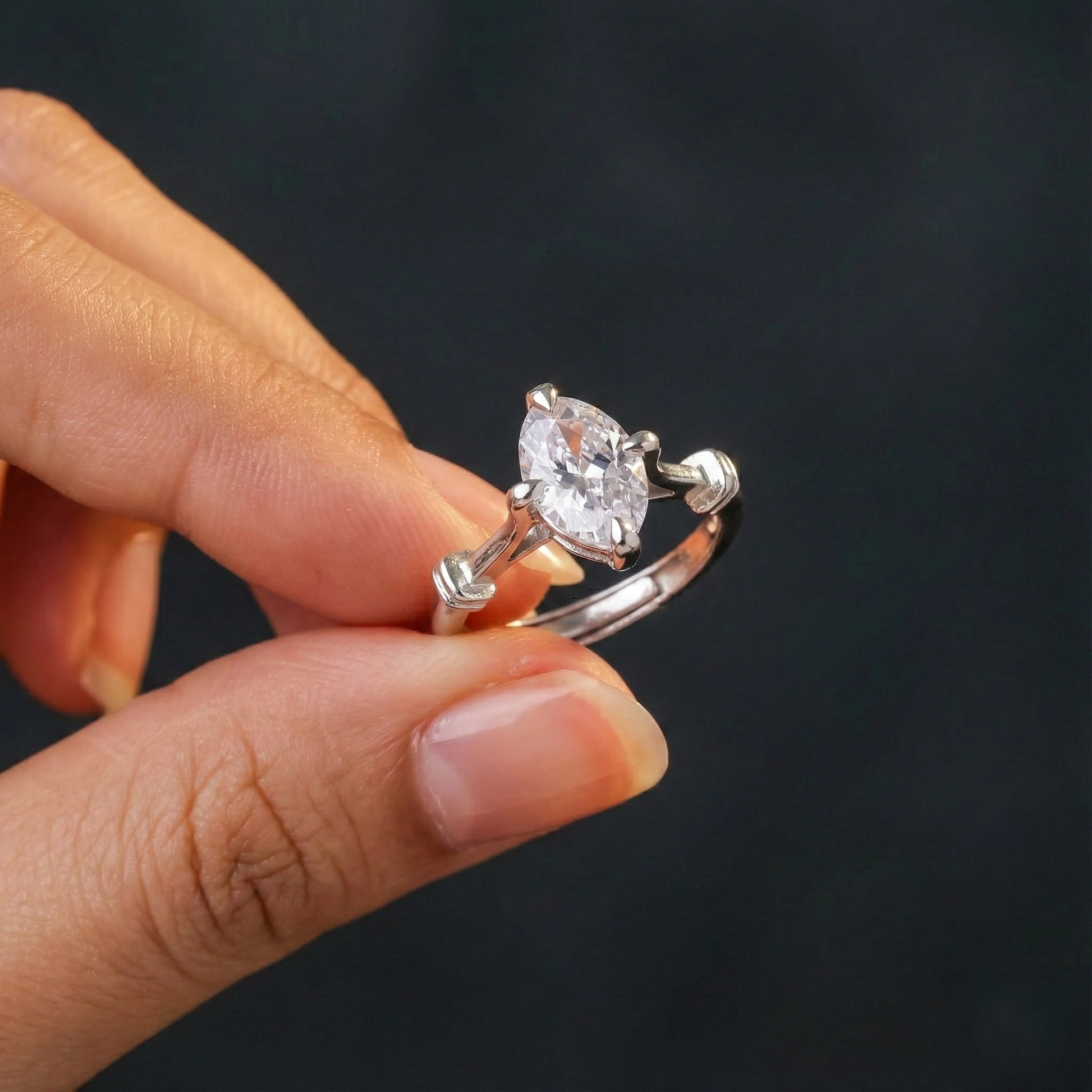 Silver ring with a heart-shaped diamond held by a hand against a dark background