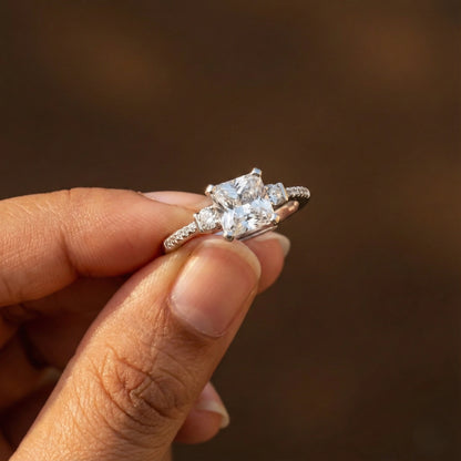 Diamond ring held between fingers against a blurred background