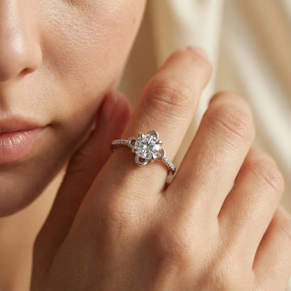 Close-up of a hand wearing a silver ring with a diamond on a neutral background