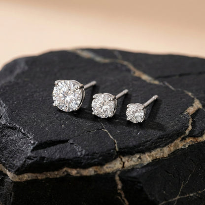 Different sizes of round silver stud earrings arranged in a straight line
