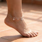Silver anklet with snowflake charms on a foot against a blurred background