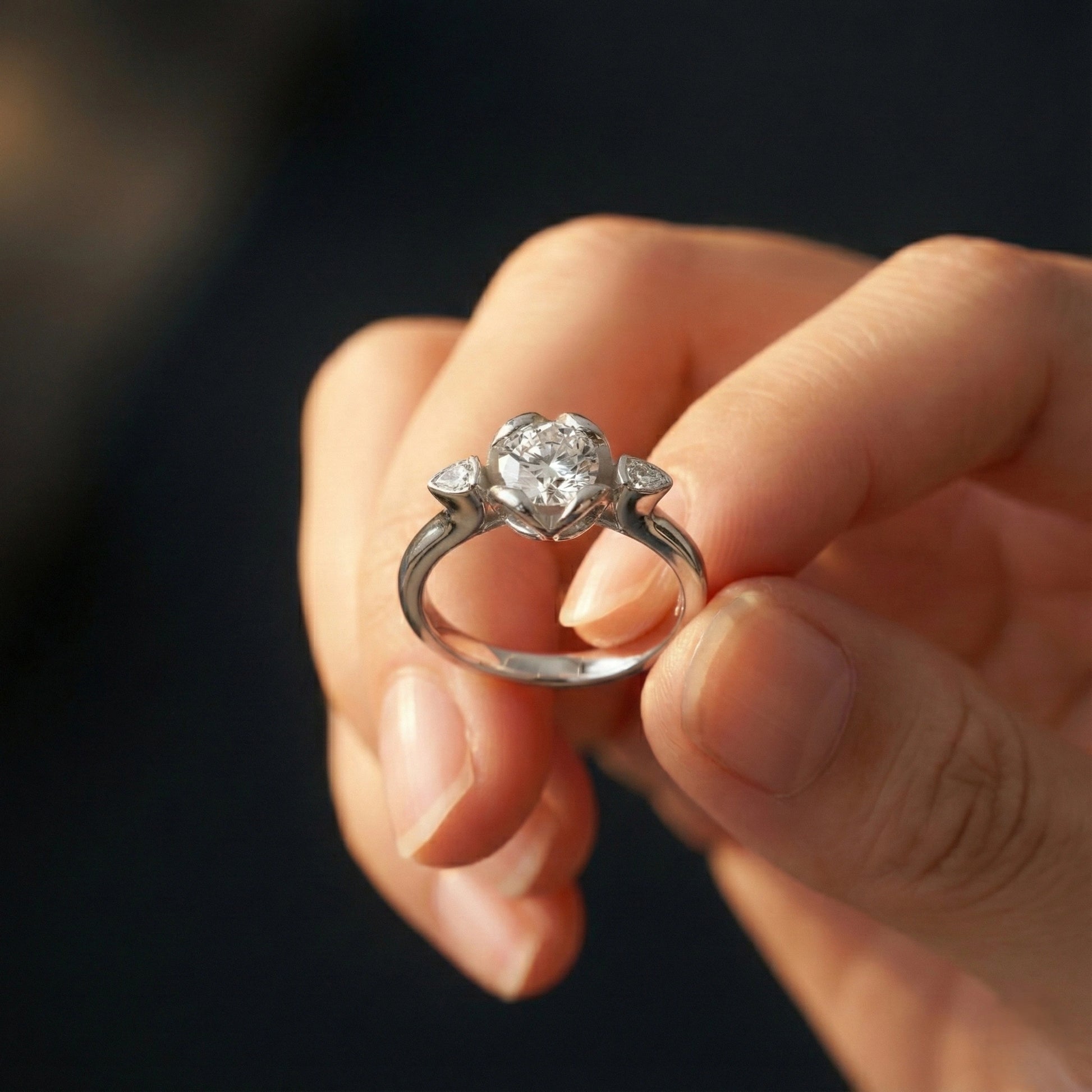 Silver ring with a diamond held between fingers against a dark background