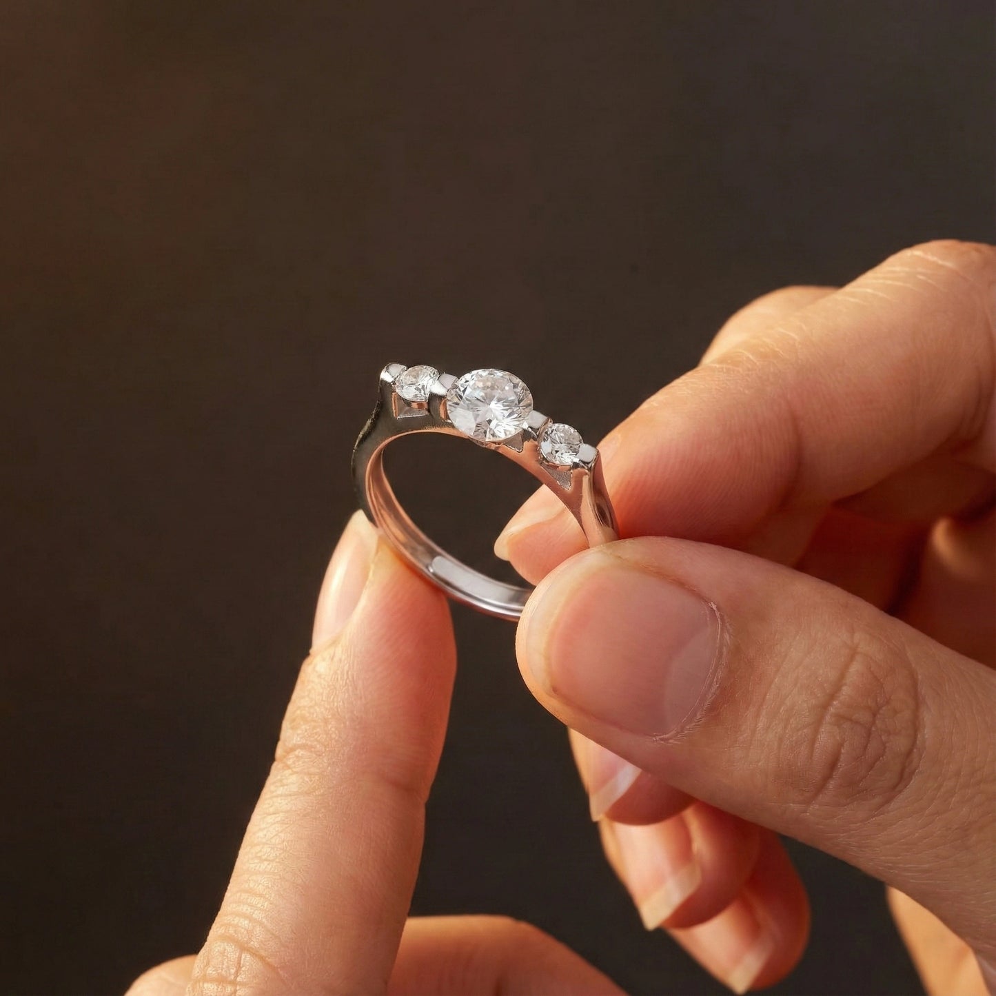 Hand holding a silver ring with multiple diamonds against a dark background
