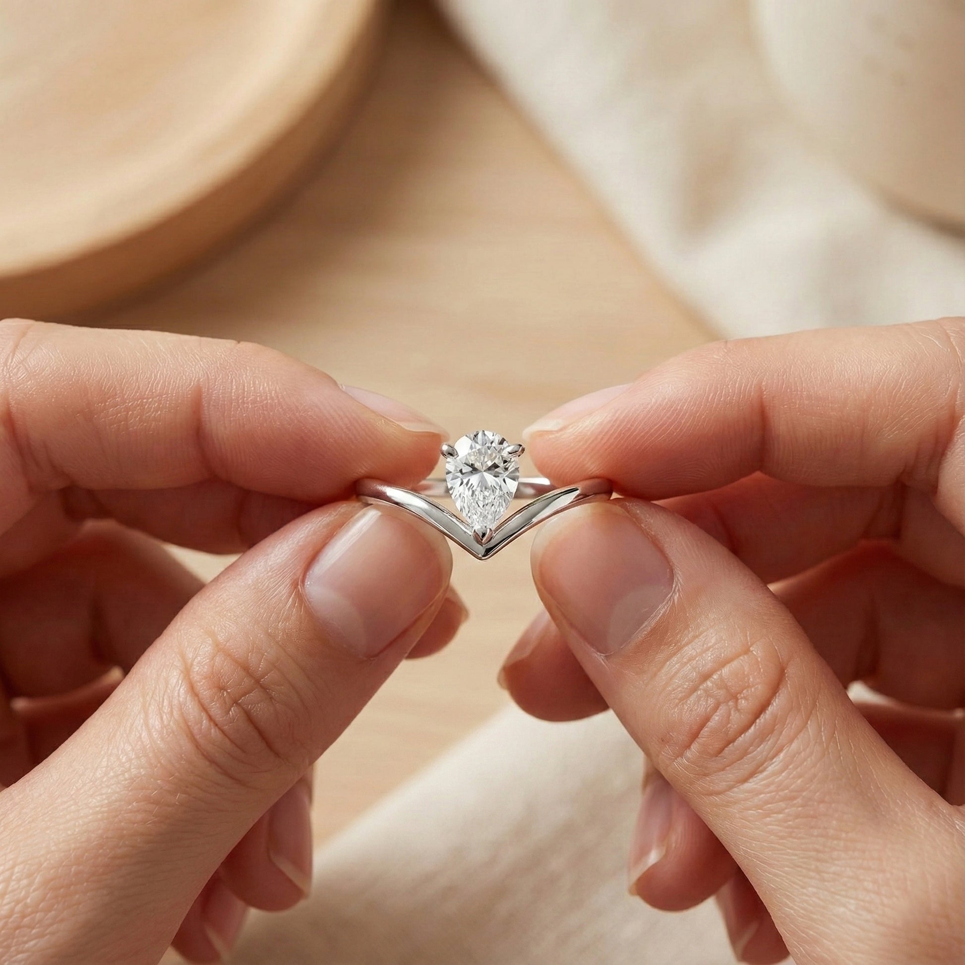 Silver ring with a heart-shaped diamond held between two fingers against a neutral background