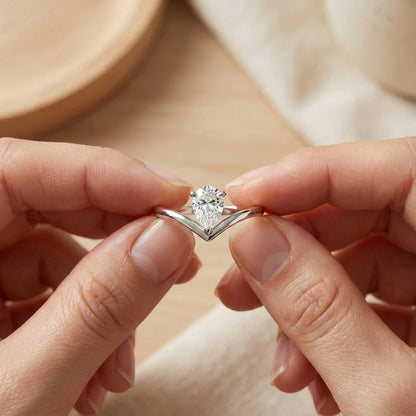 Silver ring with a heart-shaped diamond held between two fingers against a neutral background