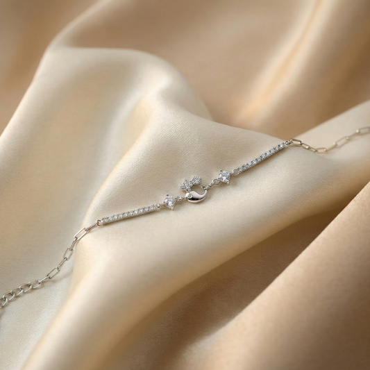 Delicate silver bracelet with star and moon charms on a beige fabric background