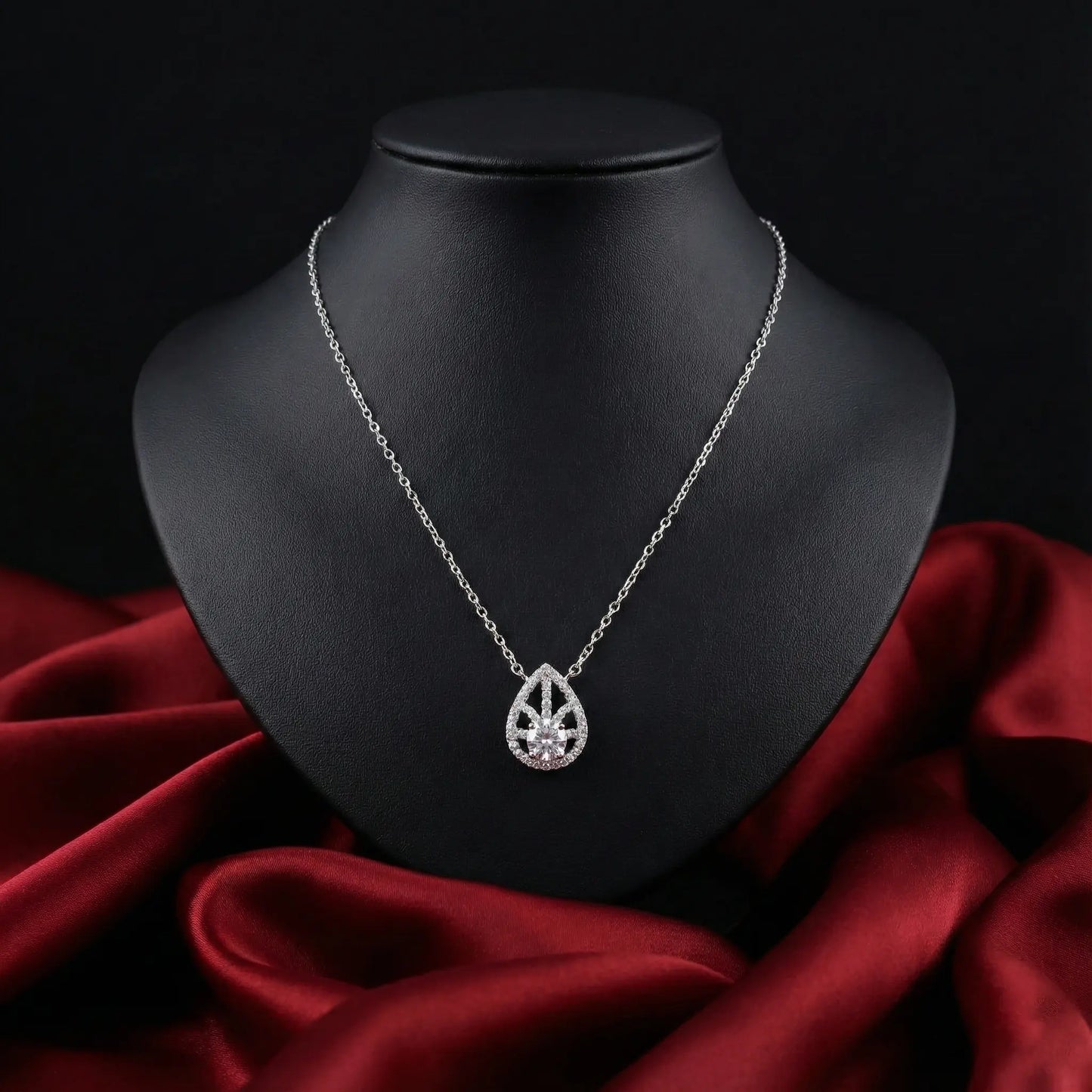 Silver necklace with a teardrop pendant on a black mannequin bust against a red fabric background