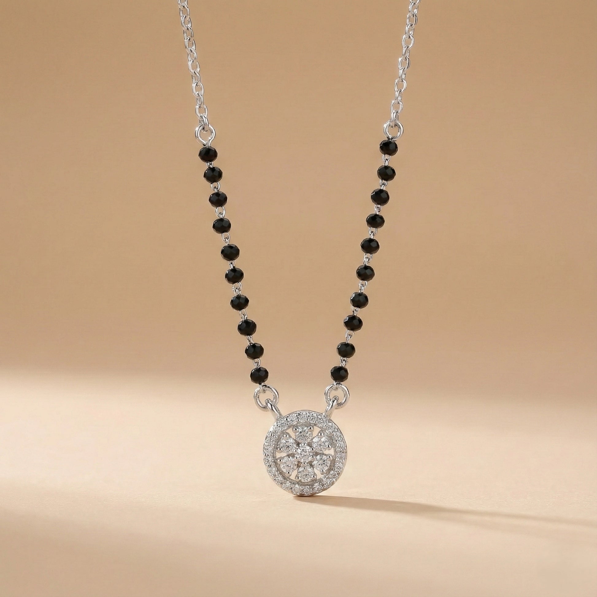 Necklace with black beads and a silver pendant on a beige background