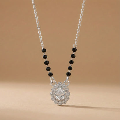 Necklace with black beads and a silver pendant on a beige background