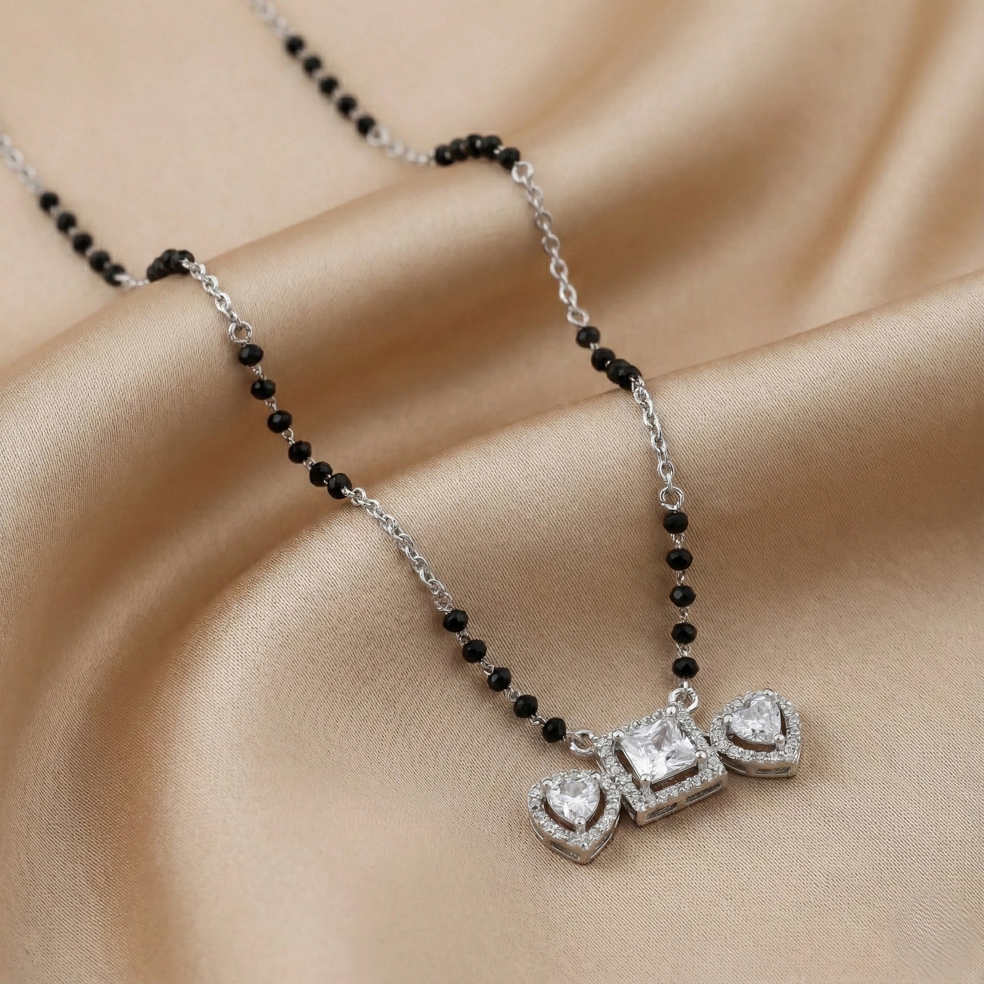 Silver mangalsutra with black beads and three pendants featuring a square center and heart-shaped sides”