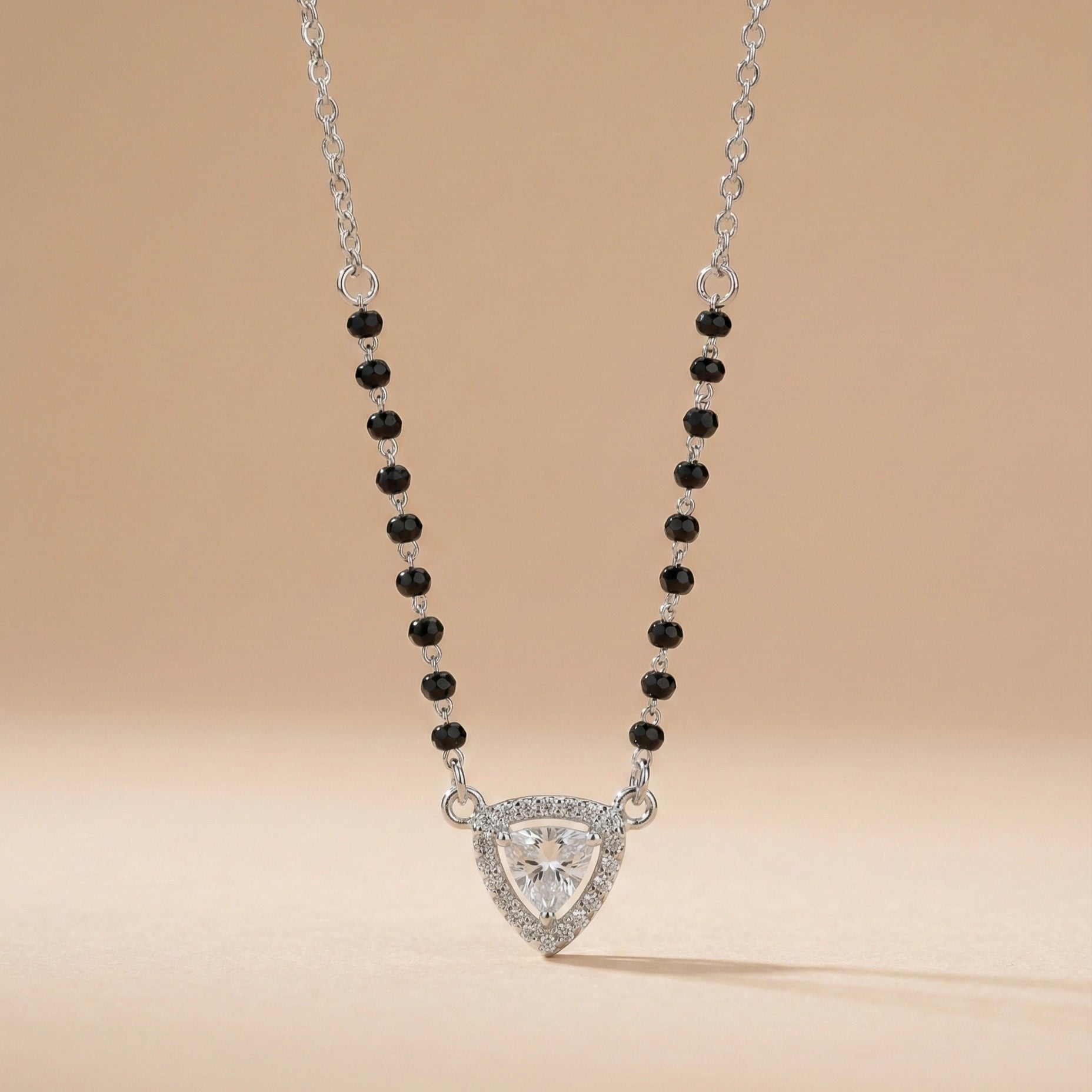 Necklace with a triangular pendant and black beads on a beige background