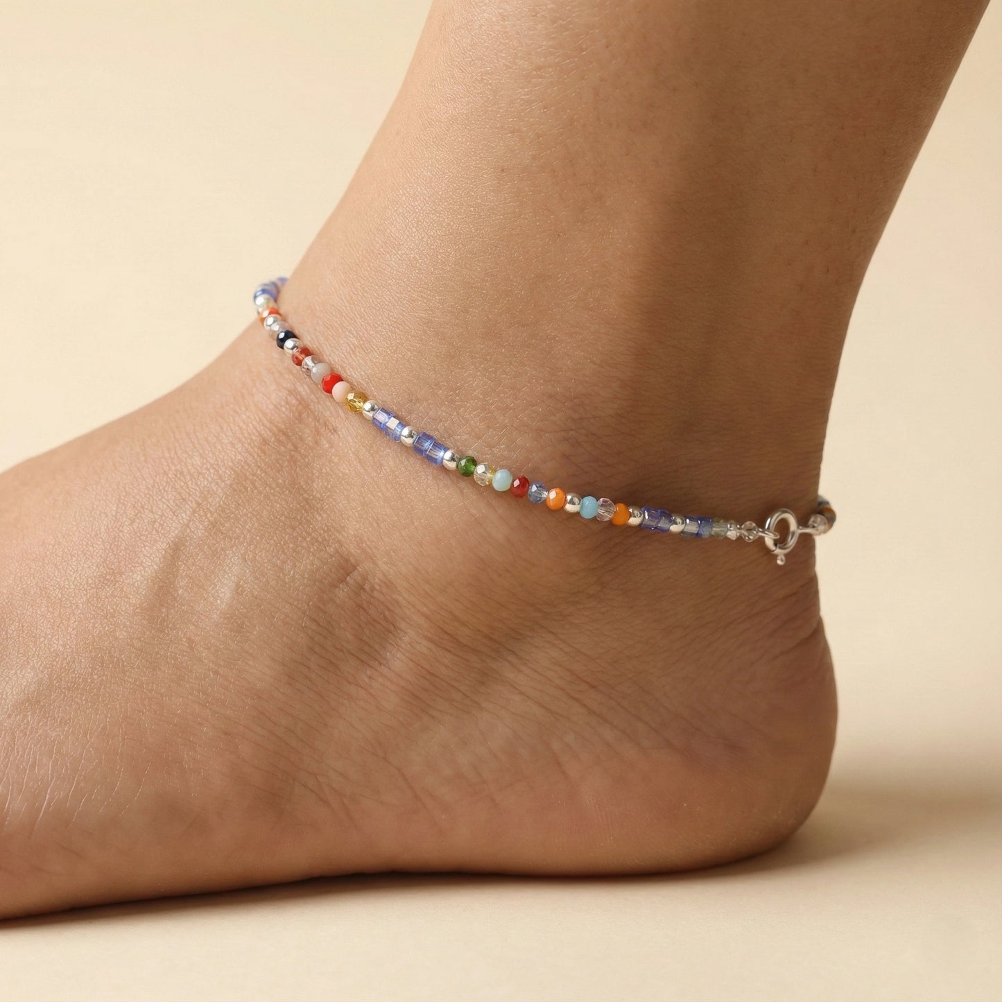 Multicolored beaded anklet on a foot against a beige background
