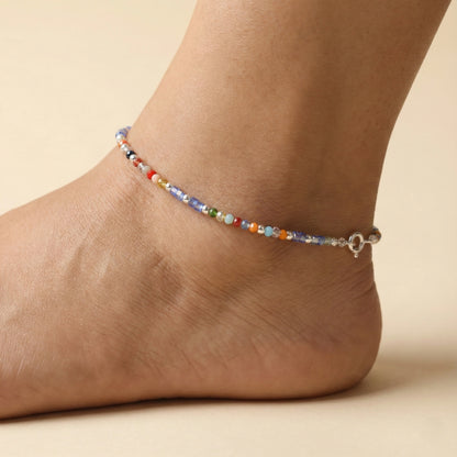 Multicolored beaded anklet on a foot against a beige background