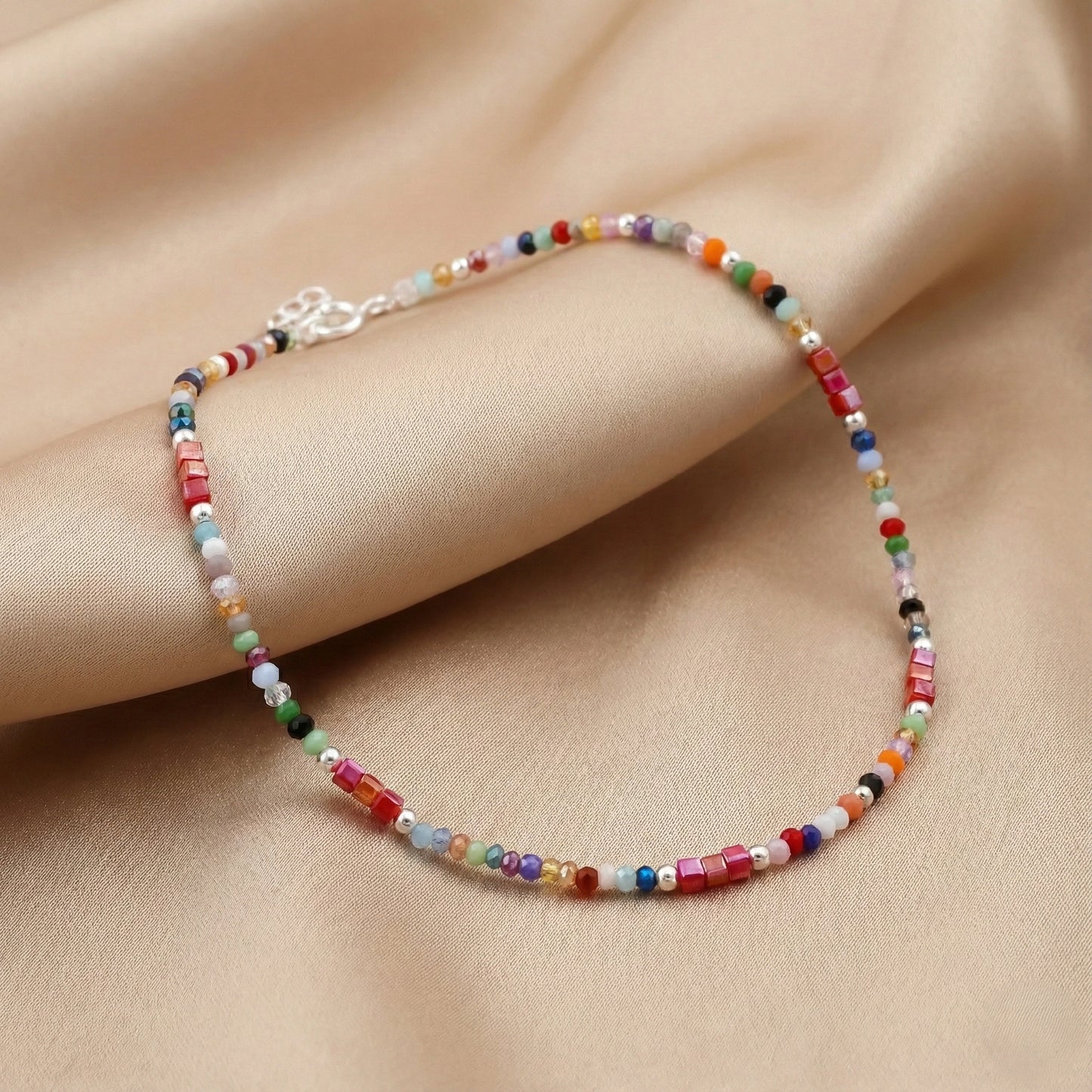 Multicolored beaded bracelet on a person's wrist against a beige fabric background