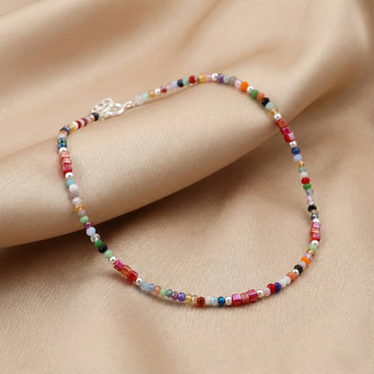 Multicolored beaded bracelet on a person's wrist against a beige fabric background